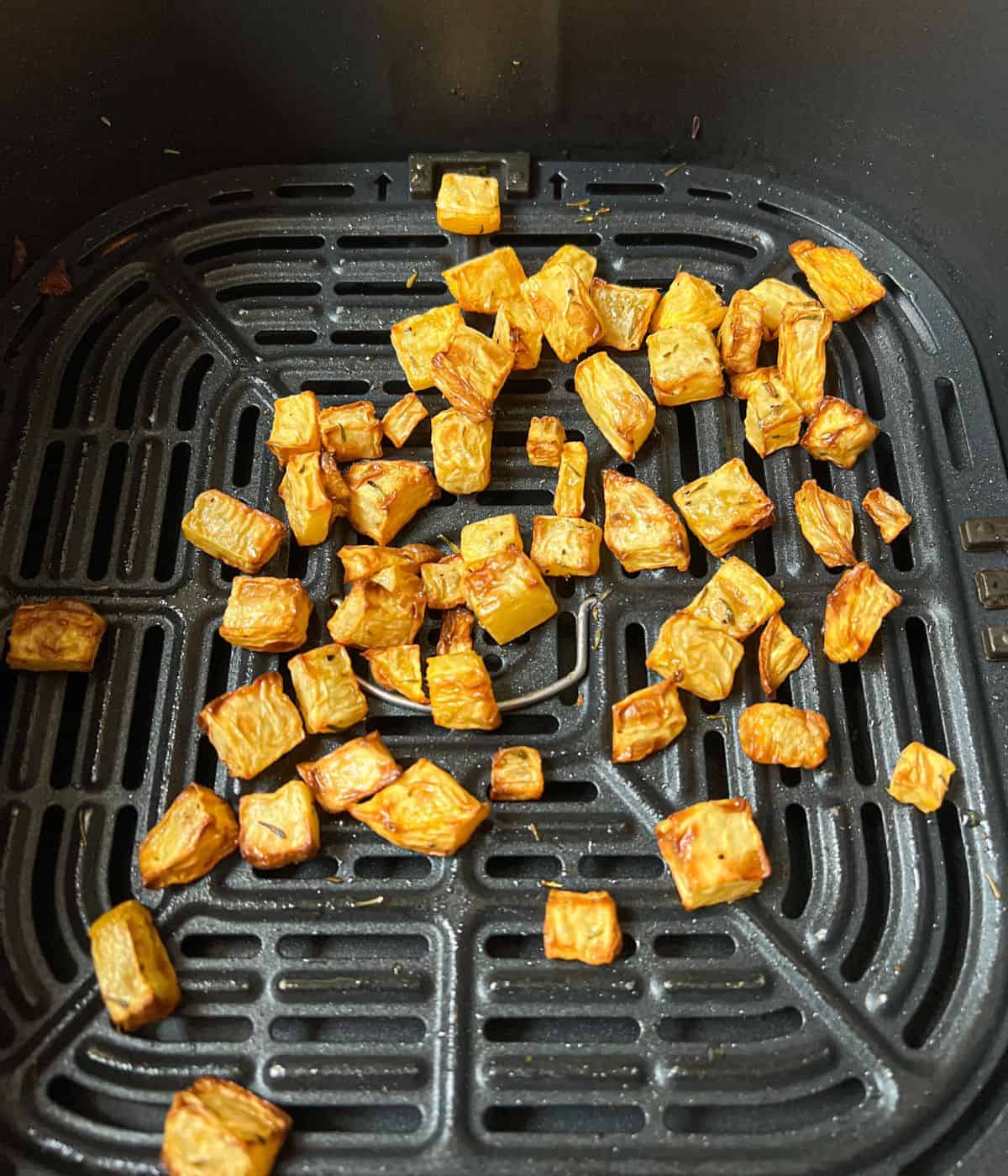 Cubes of cooked swede in an air fryer basket.