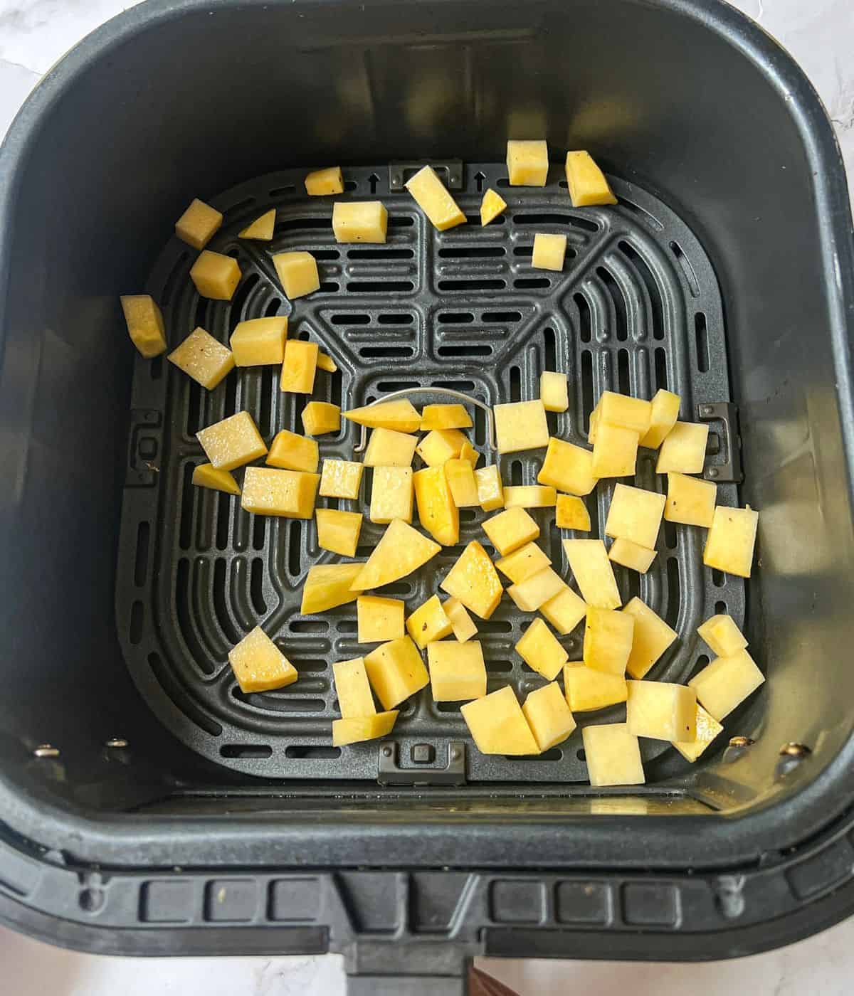 Cubes of raw swede in an air fryer basket.