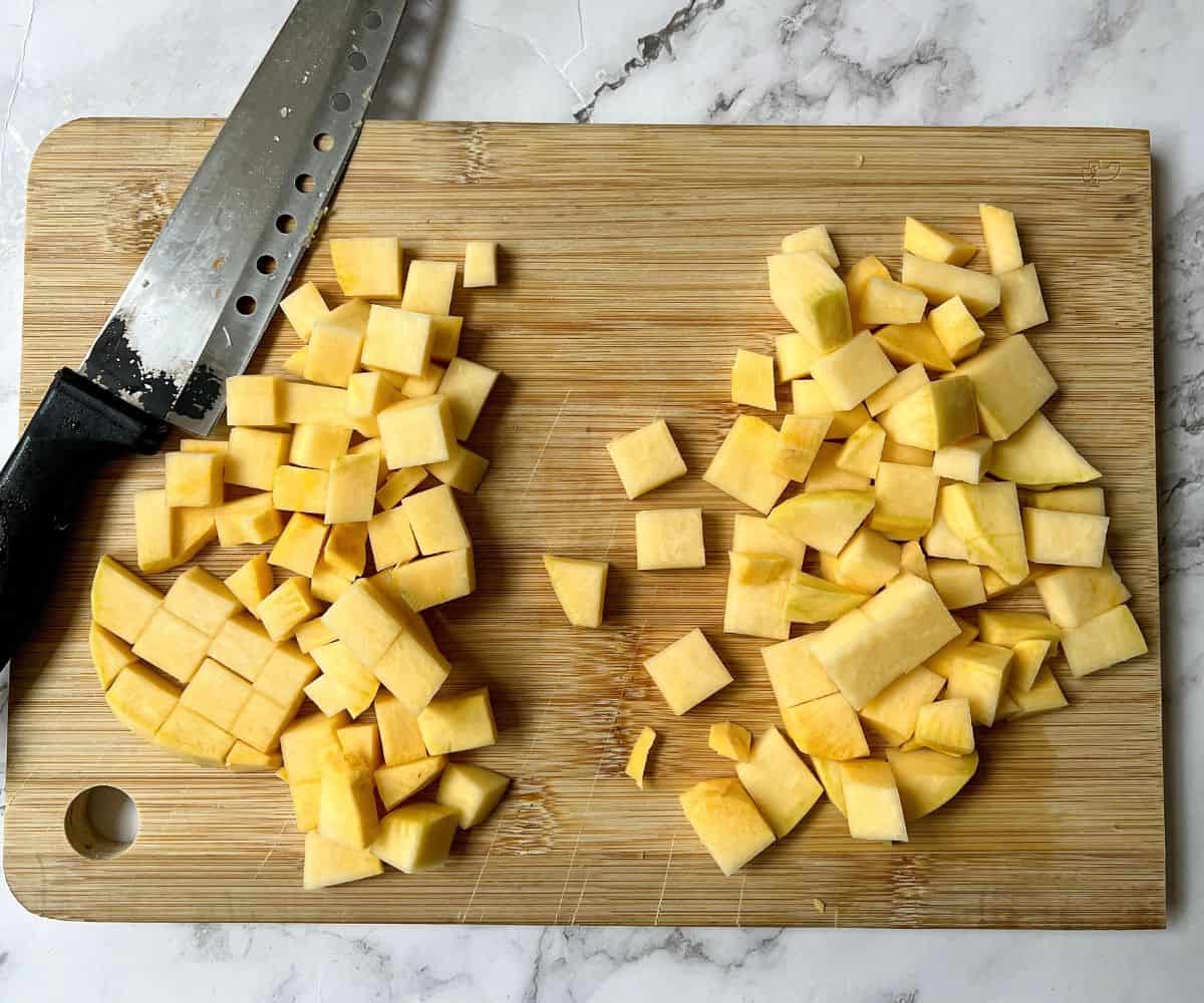 Cubes of swede on a wooden chopping board. There is also a knife on the chopping board.
