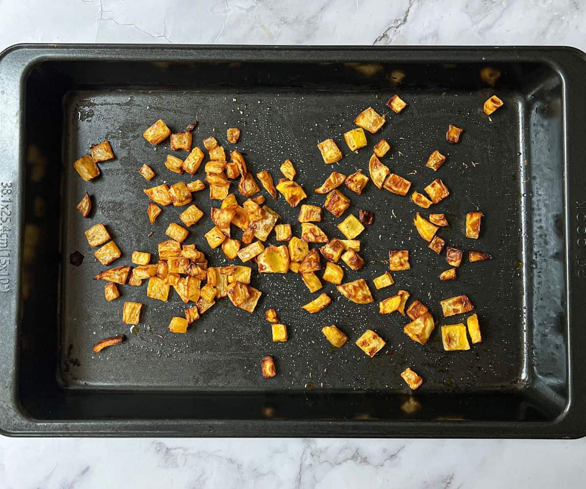 Roasted cubes of swede on a black rectangular baking tray.