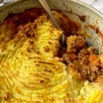 Shepherds pie with a portion removed in a casserole dish with a spoon in it.