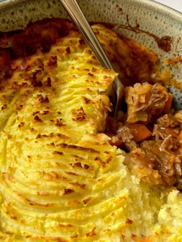 Shepherds pie with a portion removed in a casserole dish with a spoon in it.