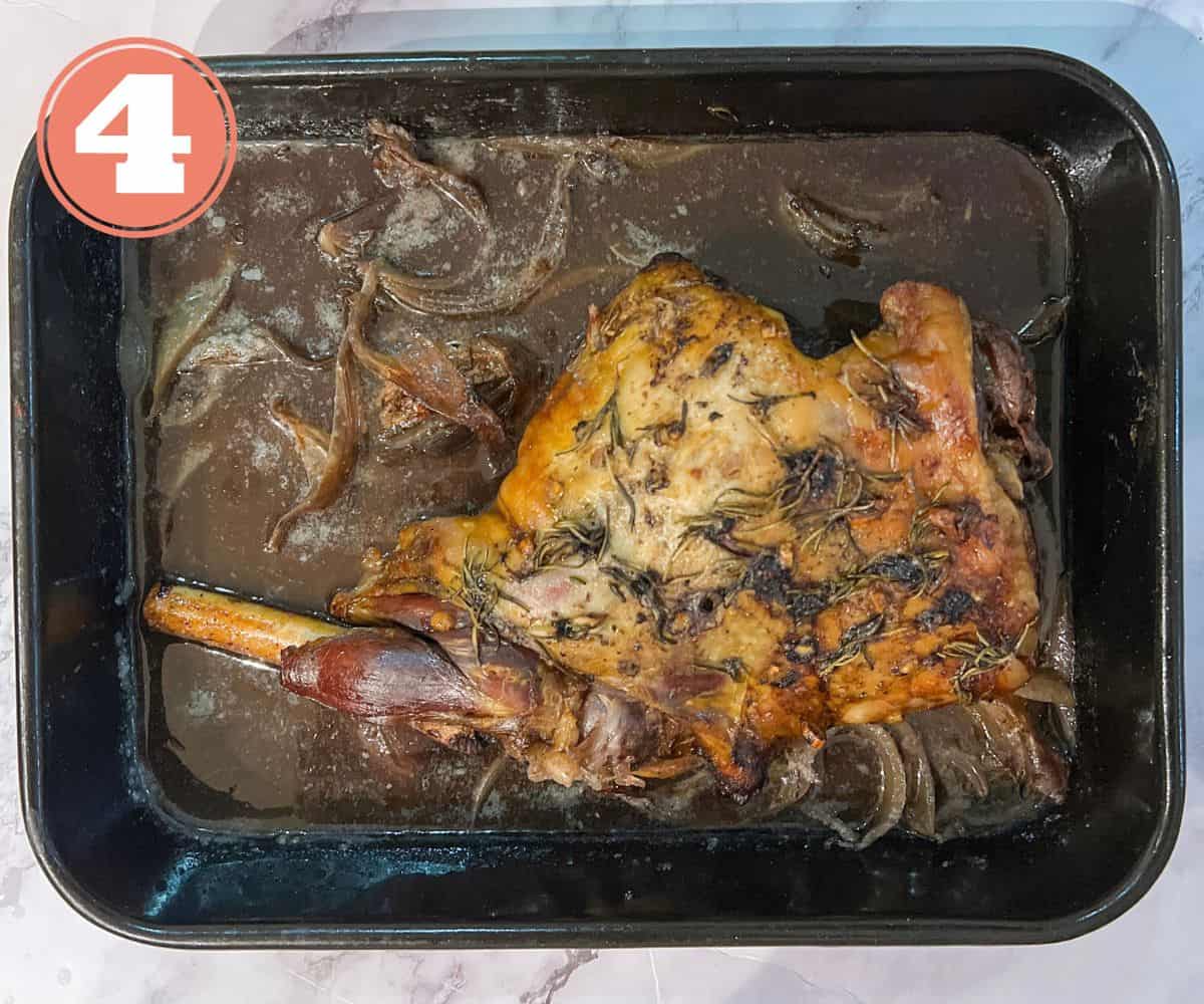 A leg of lamb, lying in gravy, garnished with rosemary in a roasting tin.