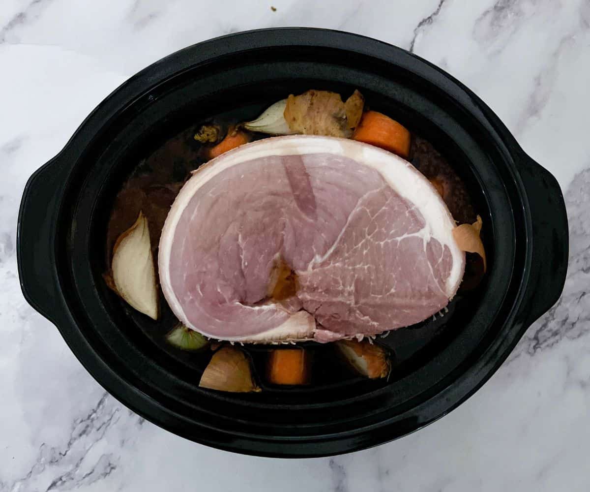 A gammon joint, onion and carrot in a slow cooker.