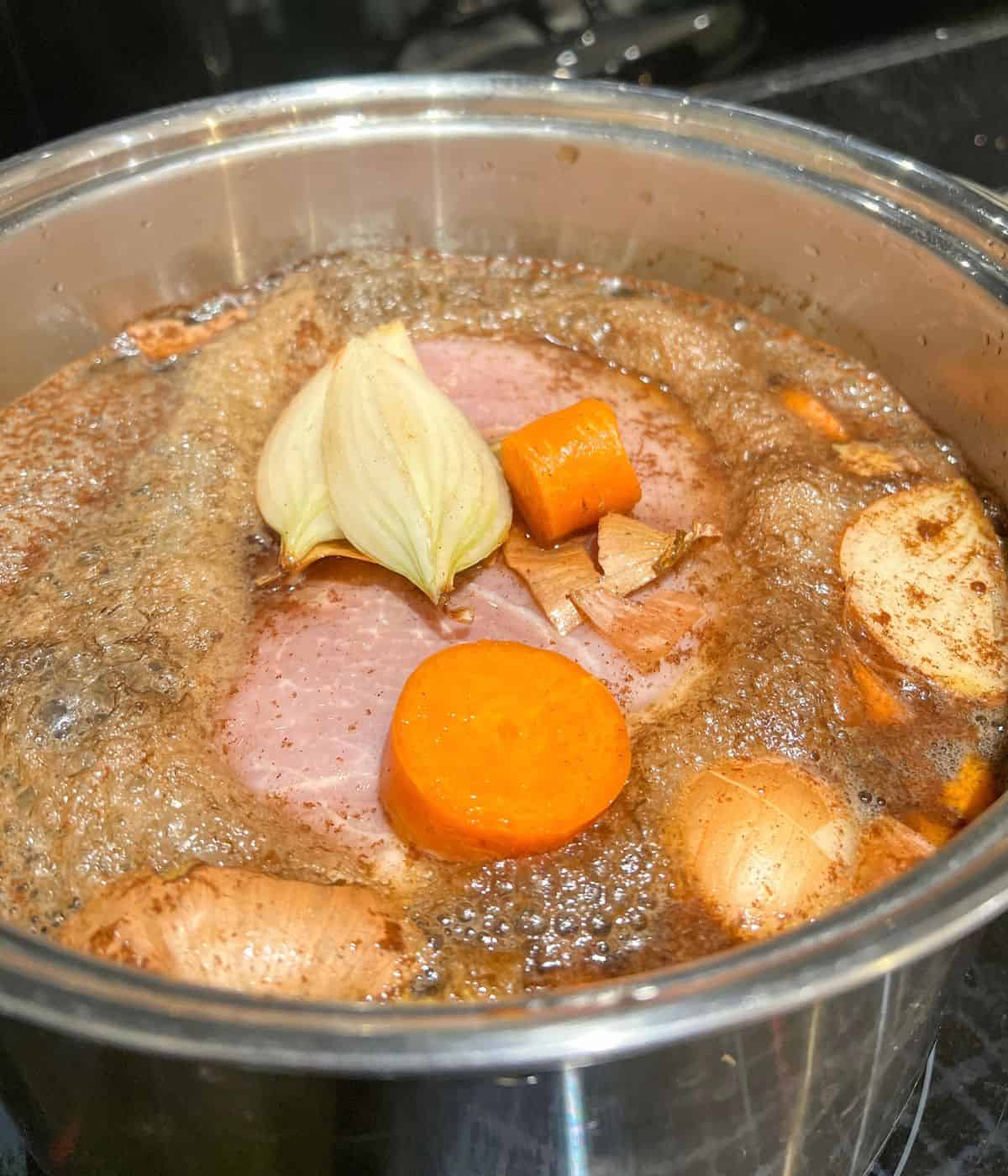 Gammon boiling in a saucepan with carrot and onion.