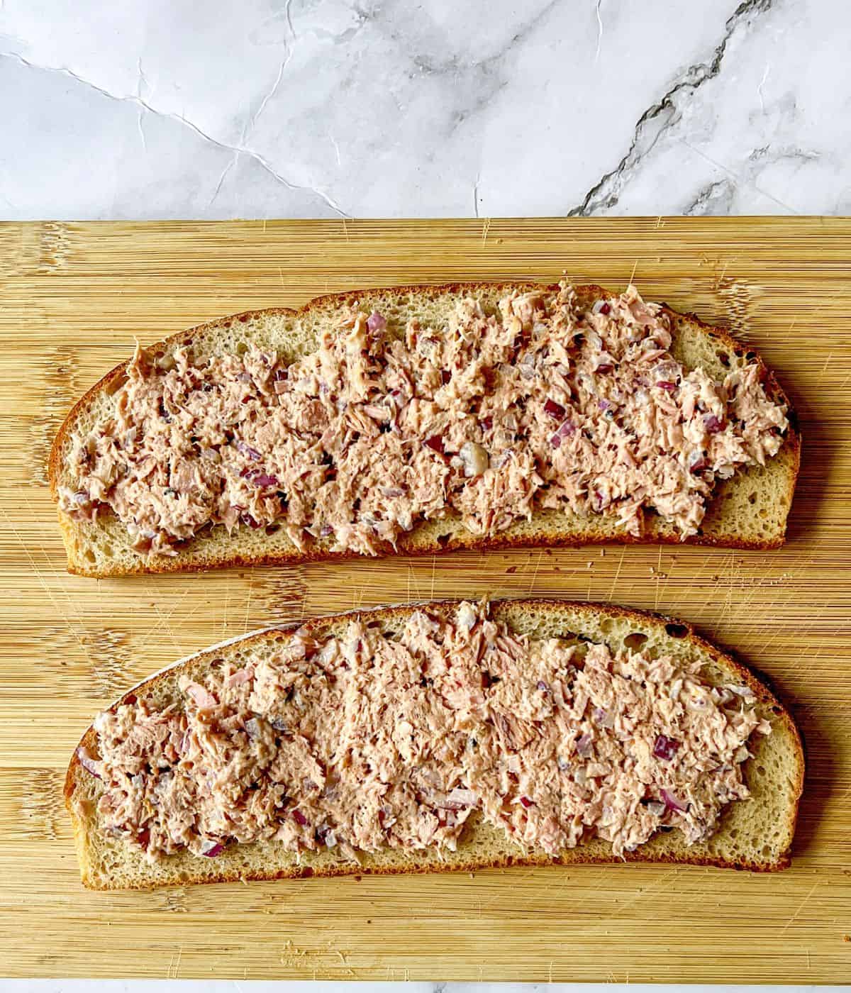 Tuna mayo spread on two slices of bread laid on a chopping board.