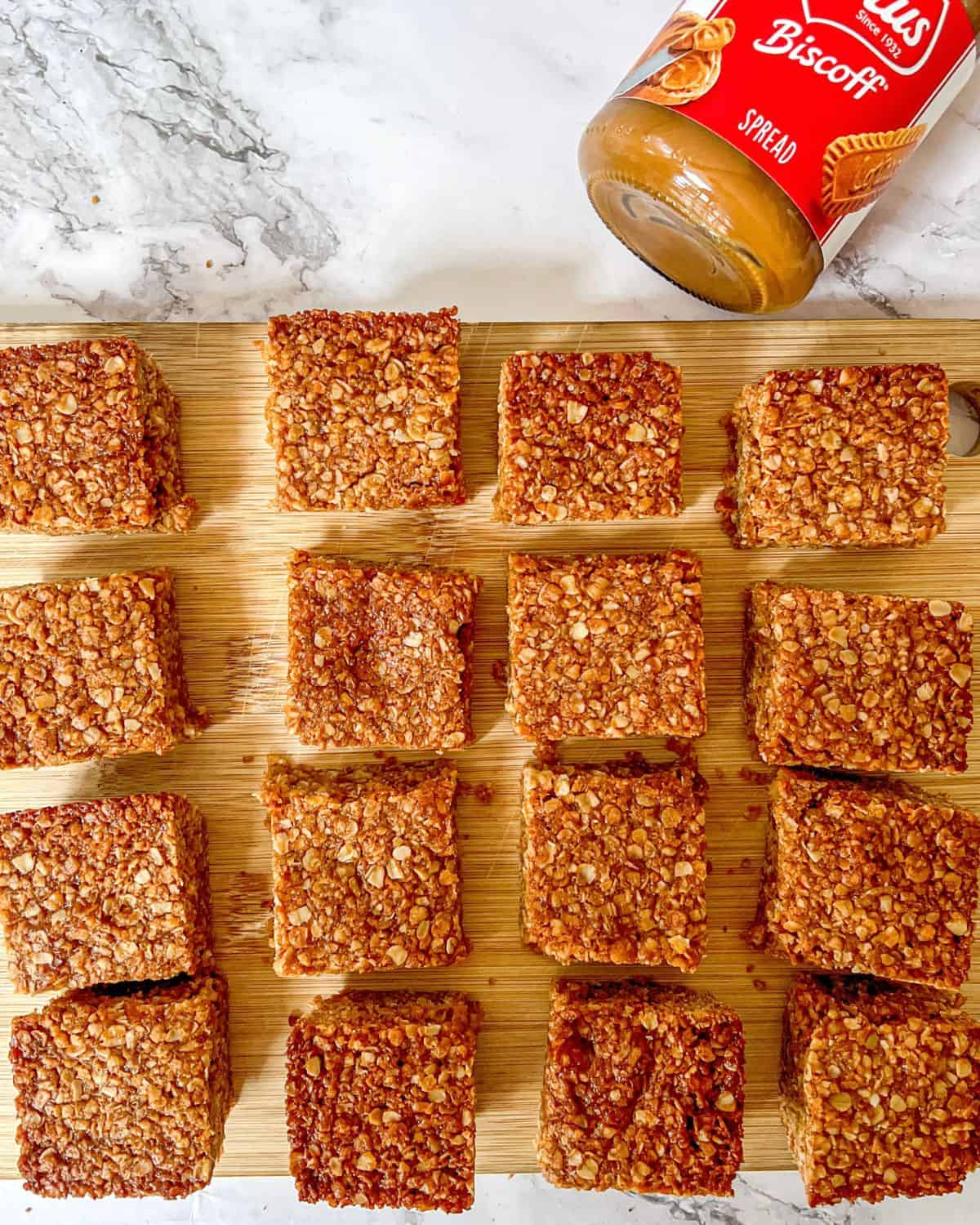 Flapjack squares laid out on a wooden chopping board with a jar of biscoff in the background.
