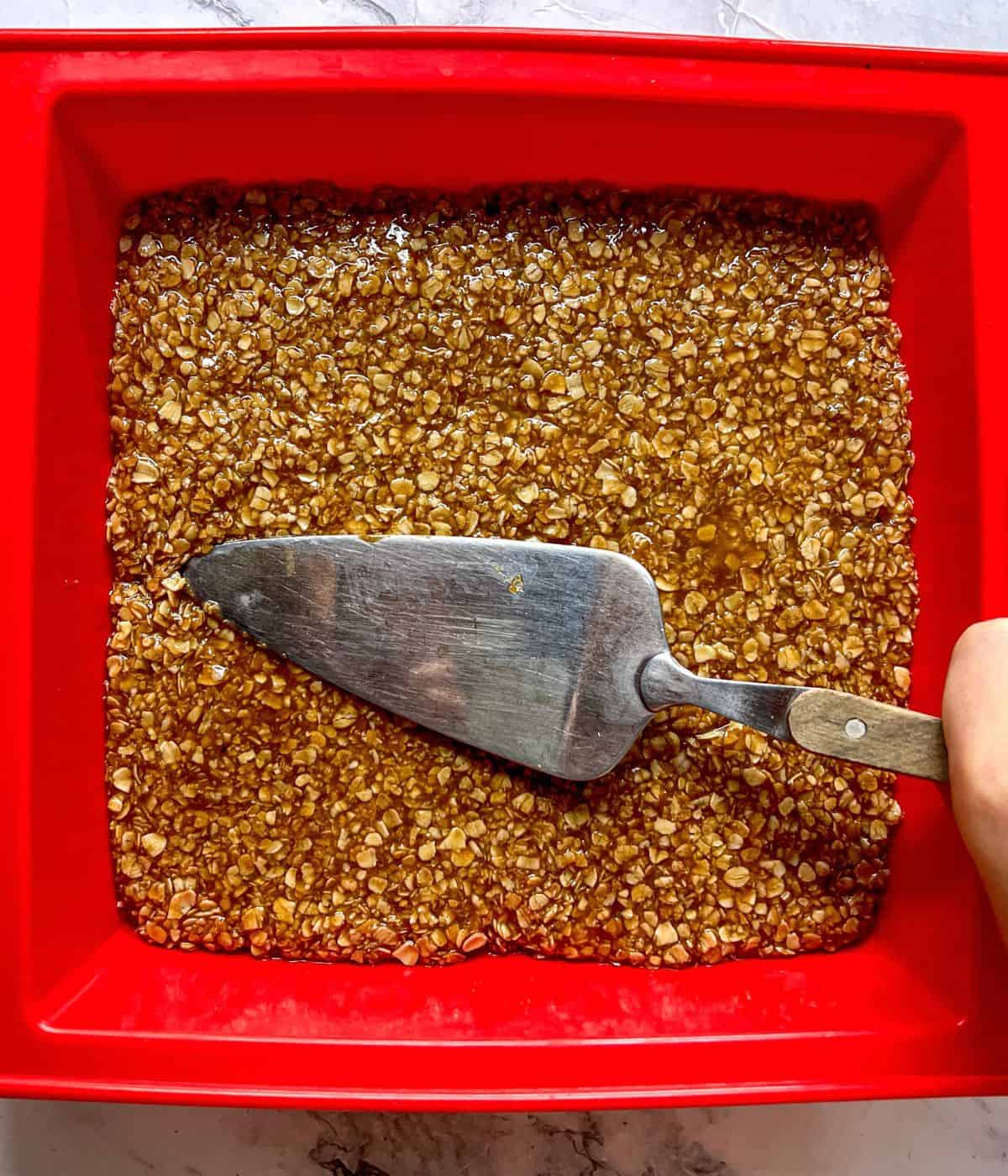 Flapjack mixture being pressed down in a silicone baking tin.