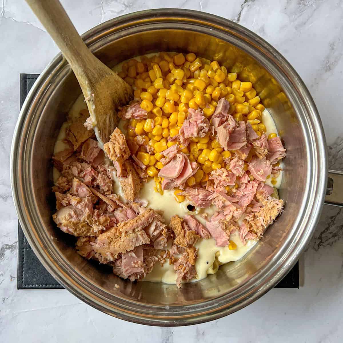 Tuna, sweetcorn and white sauce in a saucepan with a wooden spoon in it.