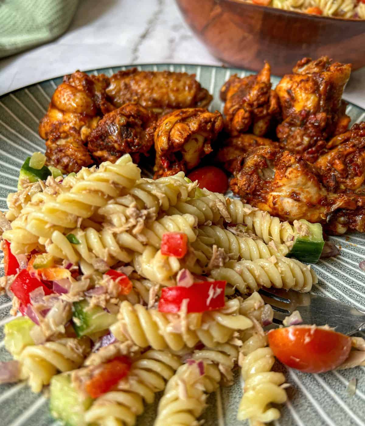 A plate containing tuna pasta salad and chicken wings.