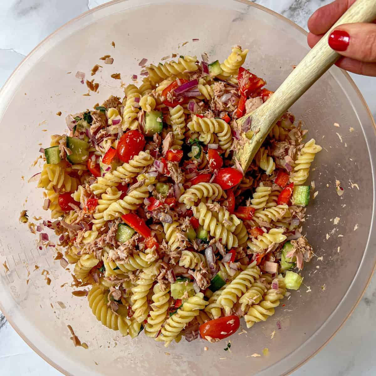 Tuna pasta salad in a large bowl being stirred with a wooden spoon.