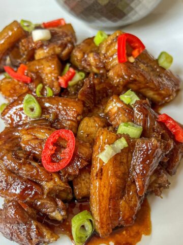Cooked pork belly in a sauce garnished with red chilli and spring onion.