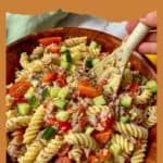 A bowl of tuna pasta salad with a wooden spoon in it.