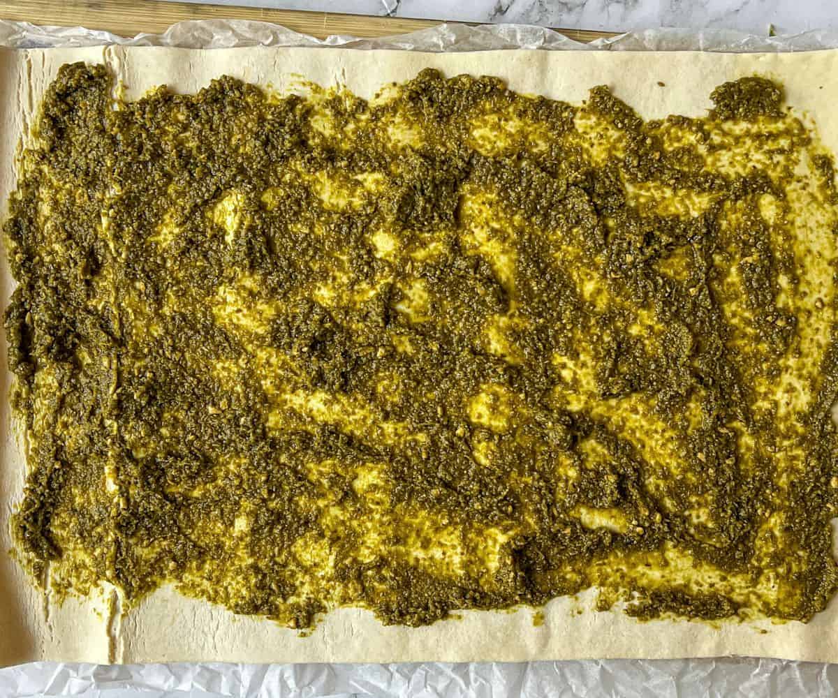 A sheet of puff pastry with pesto spread on top.