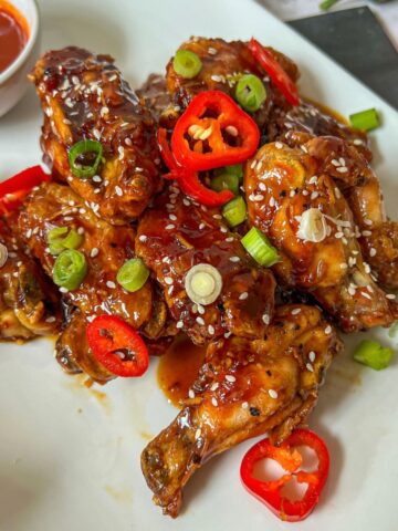 A plate of sticky chicken wings garnished with spring onion and sliced chilli.