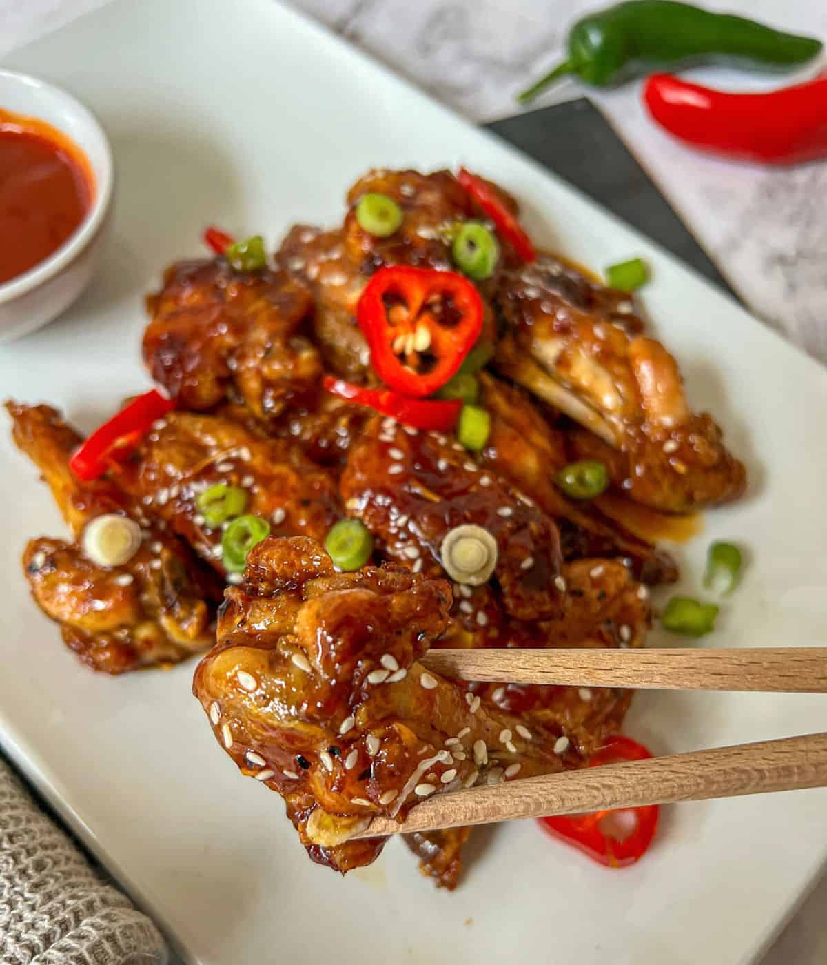 Sticky chicken wings garnished with sesame seeds are being picked up with chopsticks.