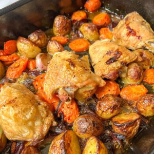 A roasting tin containing chicken thighs, carrots and potatoes.