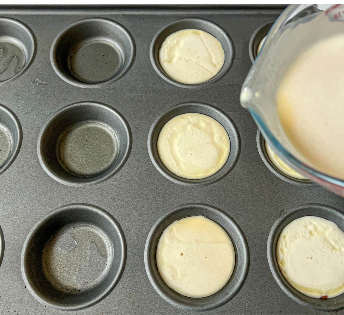 Yorkshire pudding batter being poured into a muffin tray.