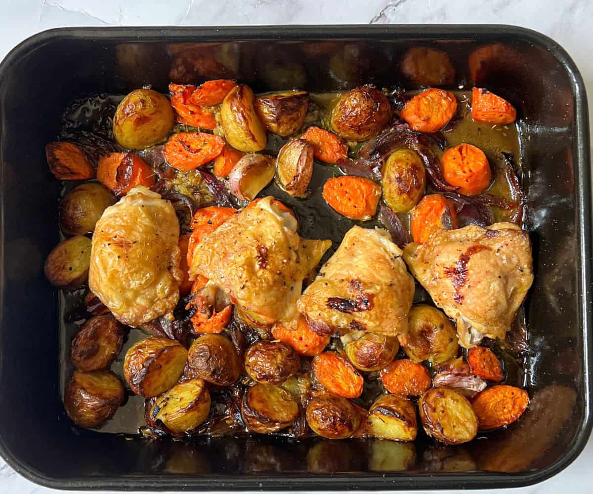 Four chicken thighs, potatoes and carrots in a roasting tin.