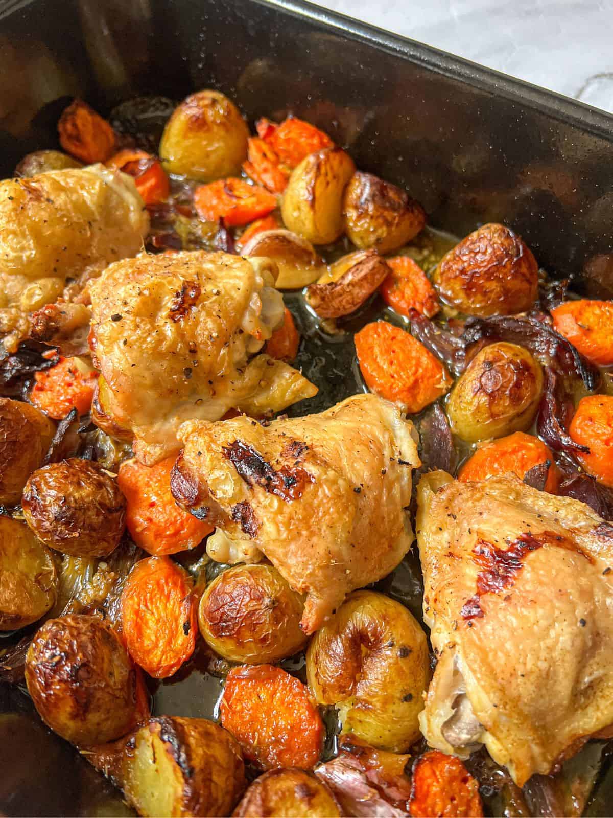 Roasted chicken thighs, carrots and potatoes in a roasting tin.