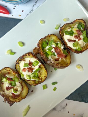 Four potato skins on a plate topped with sour cream and spring onion.