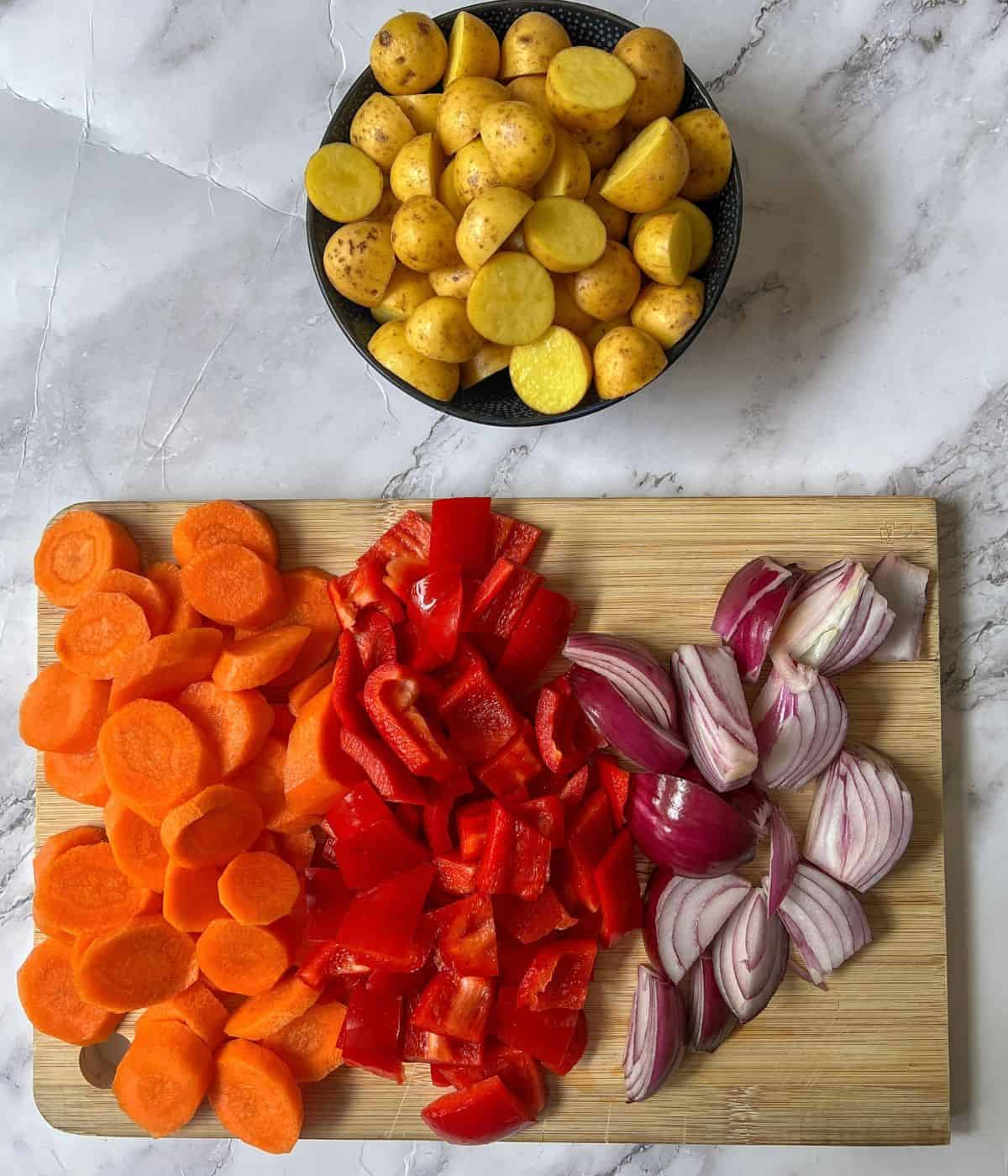 Raw, chopped carrots, red peppers, red onion and baby potatoes.
