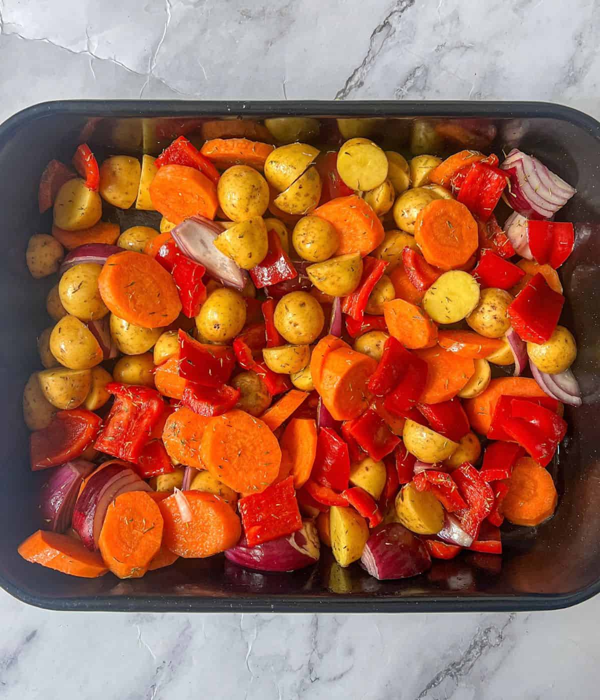 Raw potatoes, red onion, red peppers and carrots in a roasting tin.