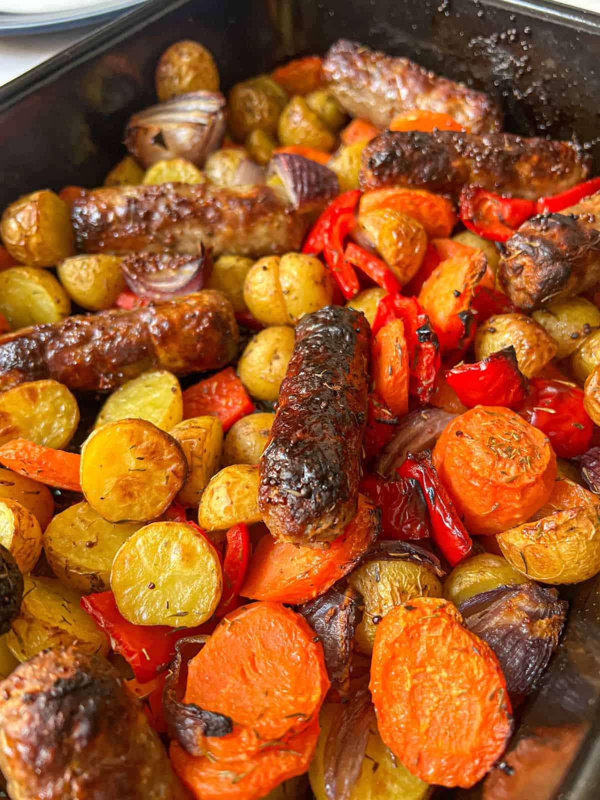 Sausages, roasted potatoes and carrots in a baking dish.