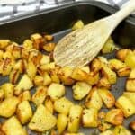 Cubed crispy potatoes in a baking tray with a wooden spoon in it.