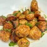 Roasted potatoes garnished with parsley in a white bowl.