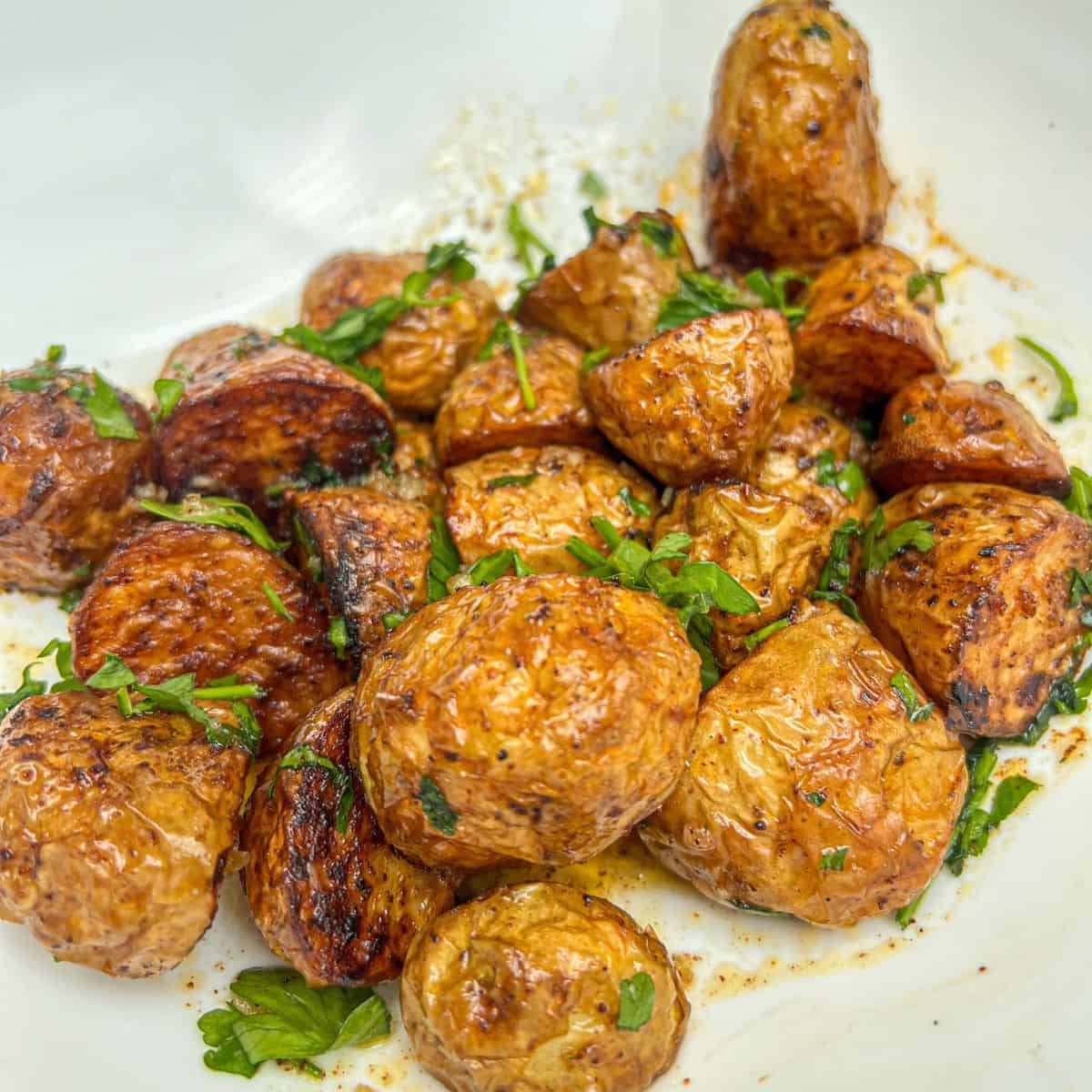 Roasted potatoes garnished with parsley in a white bowl.