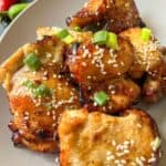 A plate containing chicken thighs garnished with sesame seeds and spring onions.