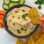 A bowl of butter bean dip with a tortilla chip being dunked into it.