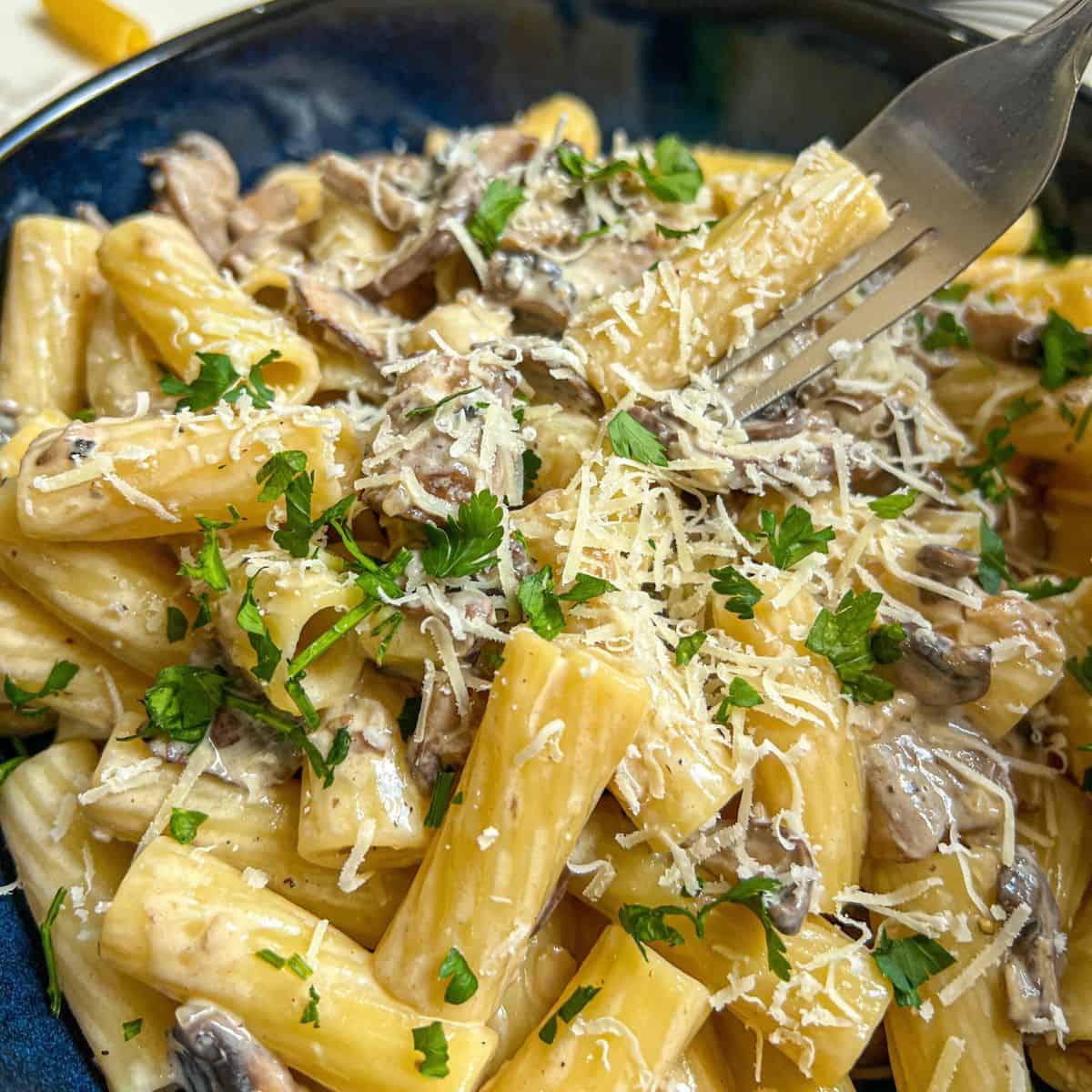 A fork being dug into a bowl of pasta topped with parmesan and parsley.