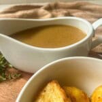 Turkey gravy in a gravy boat with a bowl of roast potatoes to the side.