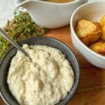 Bread sauce in a black bowl, with a bowl of roast potatoes& a gravy boat to the side.