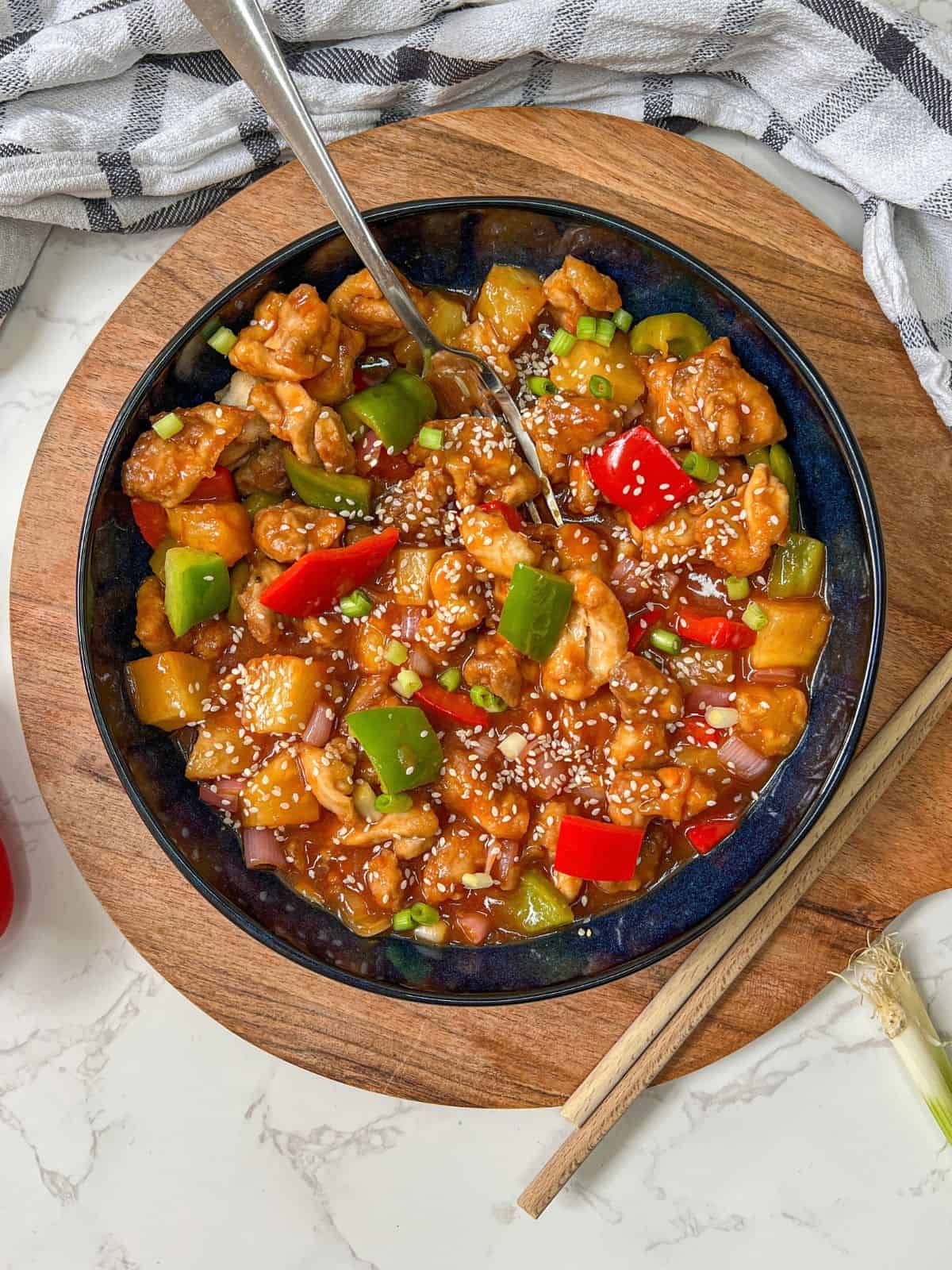 A bowl of sweet and sour chicken on a wooden board