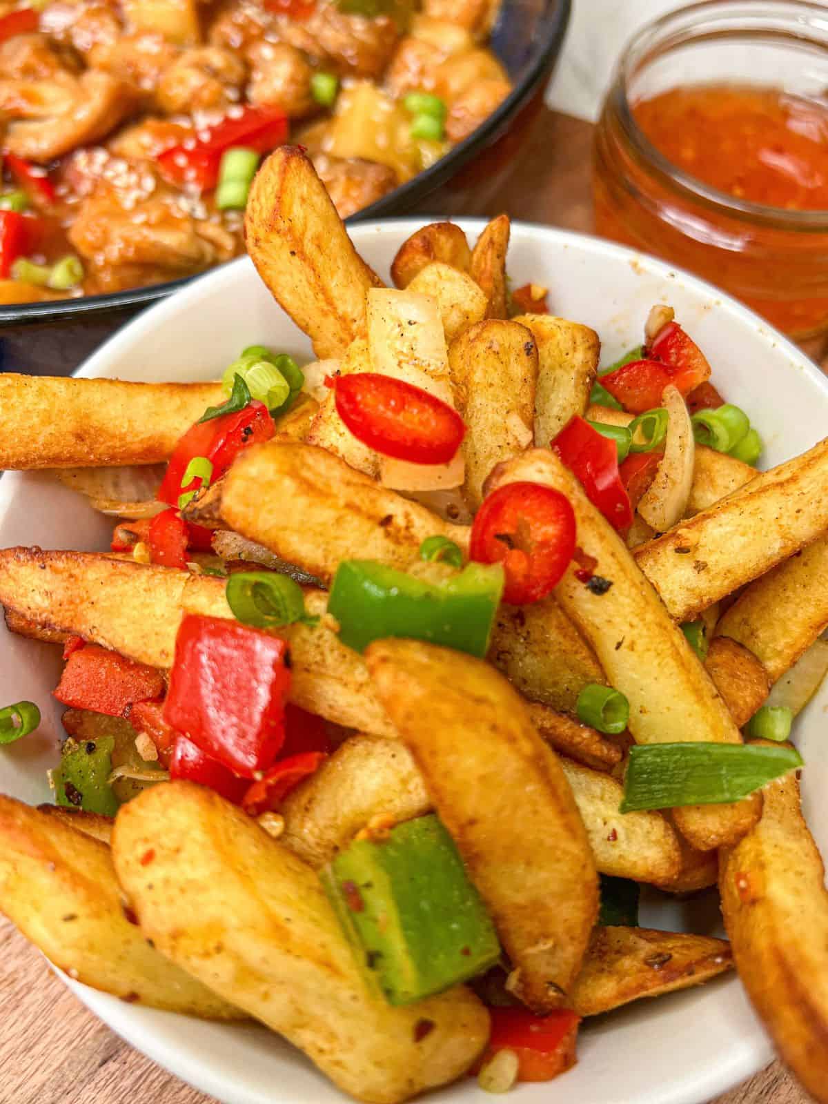 Chinese salt & pepper chips in a white bowl, garnished with red chilli.
