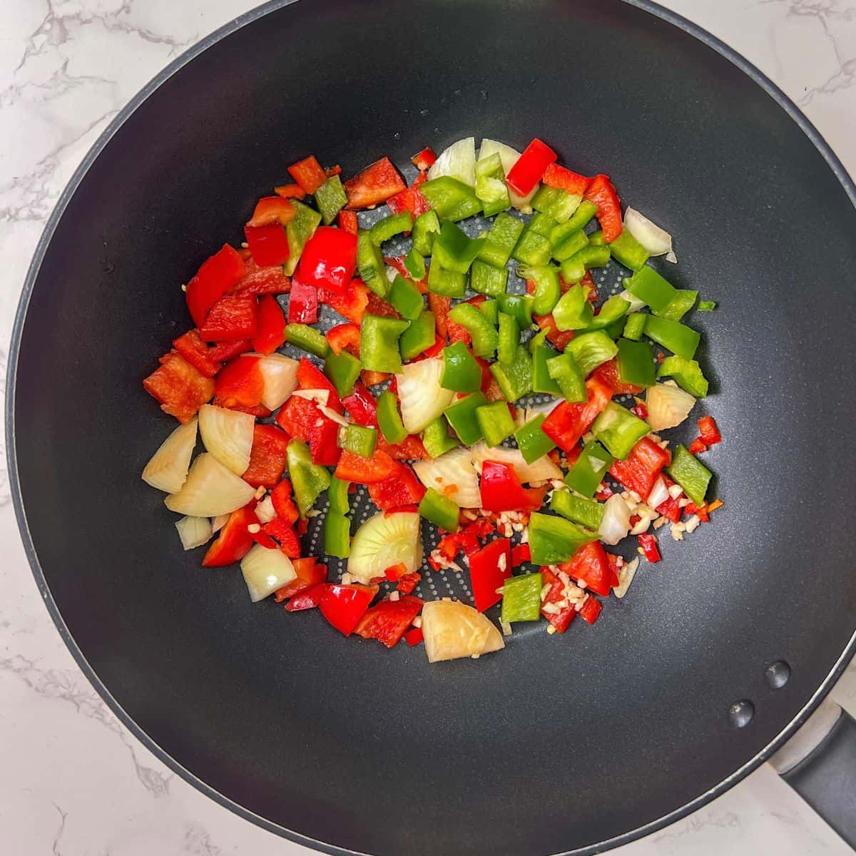 Chopped red abd green pepper and onion in a wok.