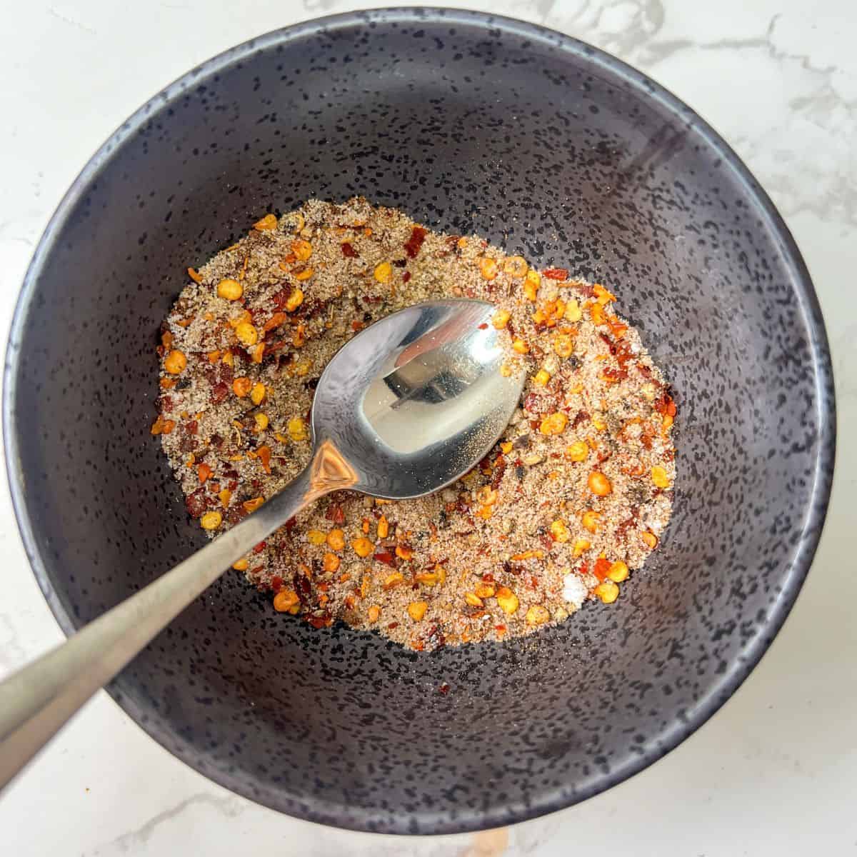 Salt & pepper spice mix in a small bowl with a teapsoon in it.