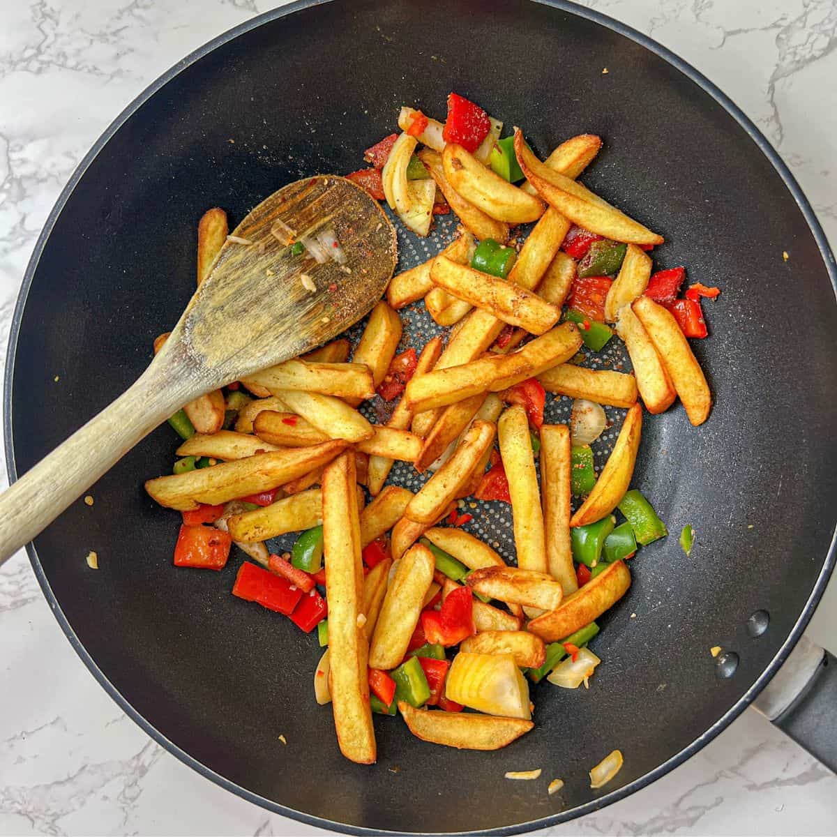 Salt & pepper chips being stirred with a wooden spoon in a wok.