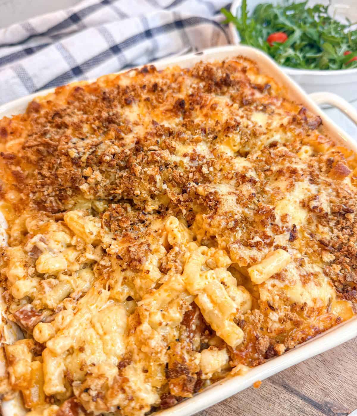 A dish containing mac and cheese with a rocket salad to the side.