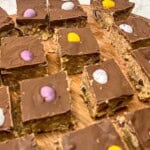 Squares of mini egg chocolate slices on a wooden board.