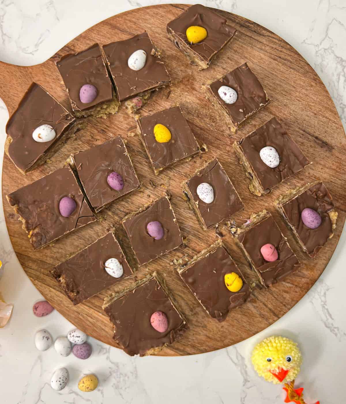 Squares of mini egg chocolate no bake slices on a wooden board.