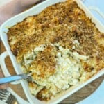 Macaroni cheese in a square dish with a serving spoon taking a portion out.