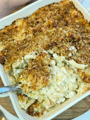 Macaroni cheese in a square dish with a serving spoon taking a portion out.