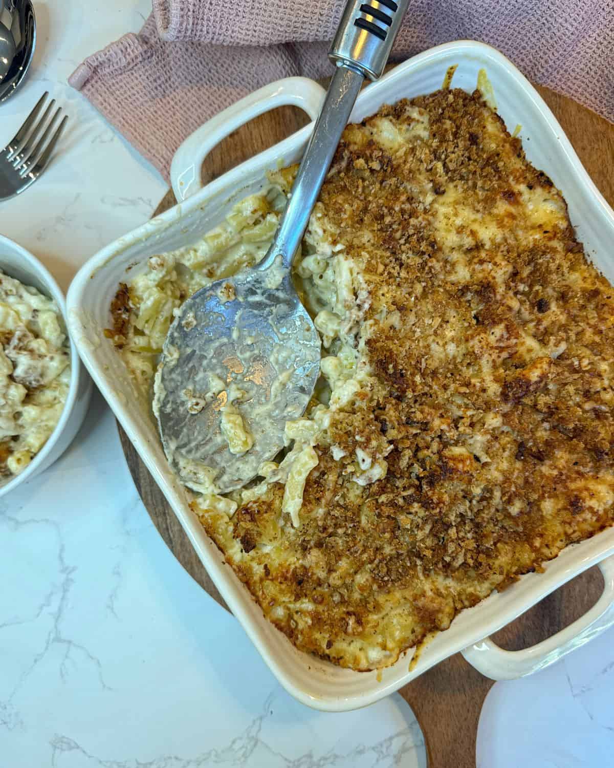 Macaroni cheese in a square dish with a serving spoon taking a portion out.