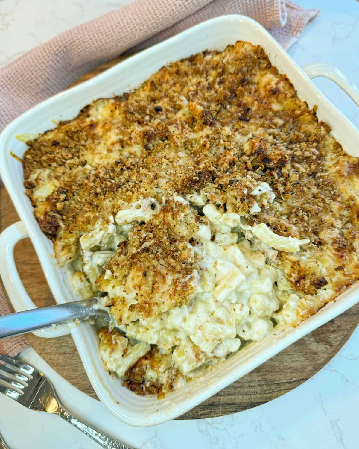 Macaroni cheese in a square dish with a serving spoon taking a portion out.