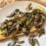 Sliced garlic mushrooms on toast sprinkled with parsley.
