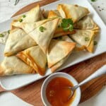A plate of samosas with some mango chutney to the side.